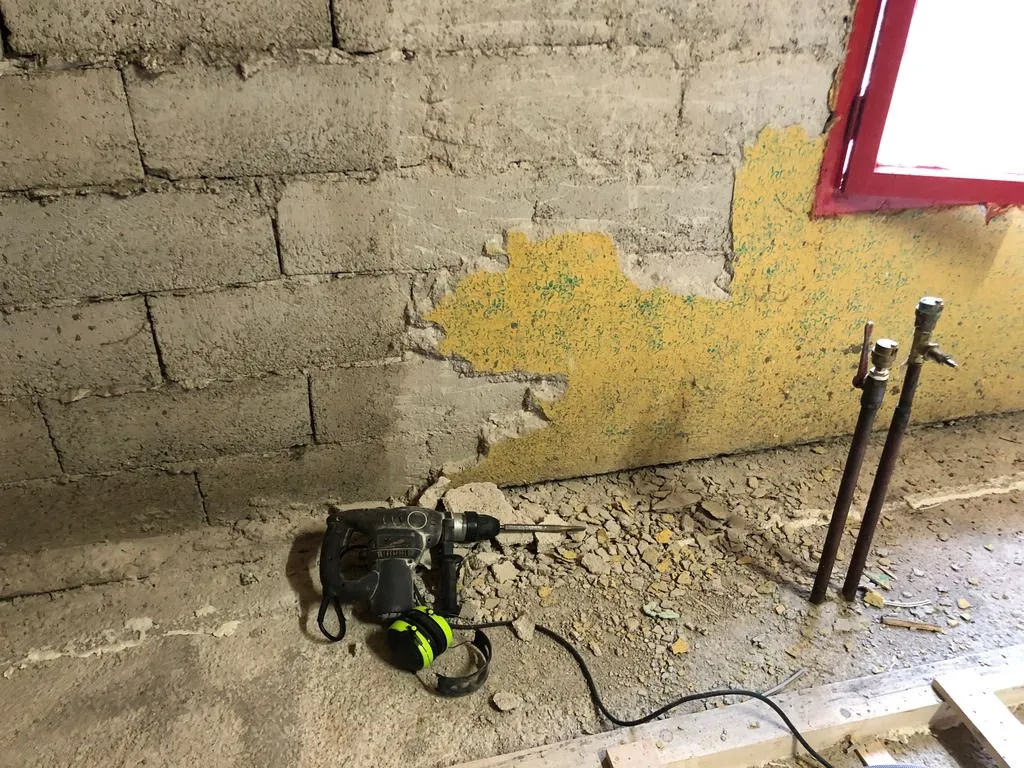 Prep work: there was an unfinished, crumbling layer of render on the west wall around the window, which we first removed with a hammer drill before addressing the bow in the wall.