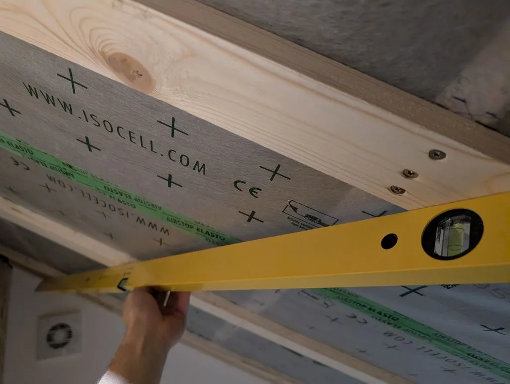 Using a straight edge to ensure the slats for the drywall are planar.