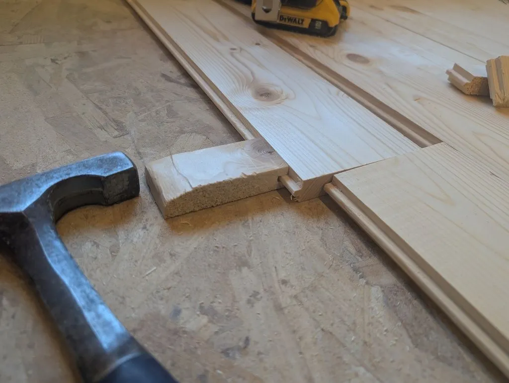 We used a simple jig made from scrap piece of flooring to fit the boards tightly. (Hitting the boards directly with a hammer would cause them to split, but the jig fits over the boards and distributes force sufficiently safely.)