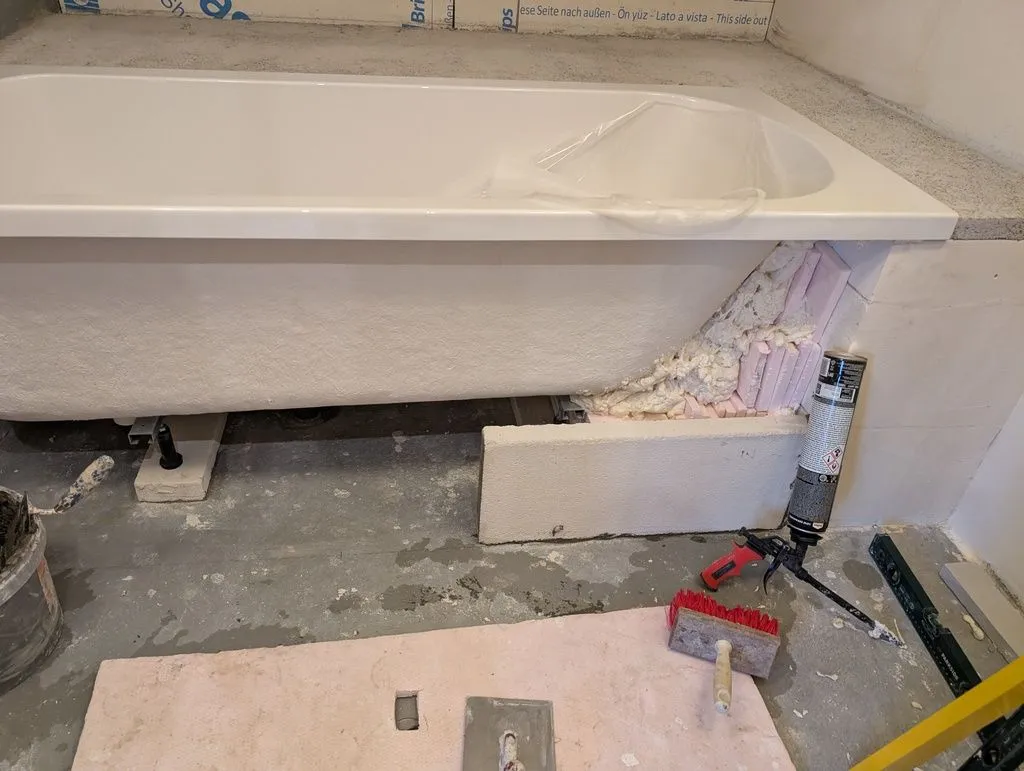 Insulating the area between the bathtub and enclosure walls with XPS and spray foam. This supports the bathtub mechanically and retains heat in the water.