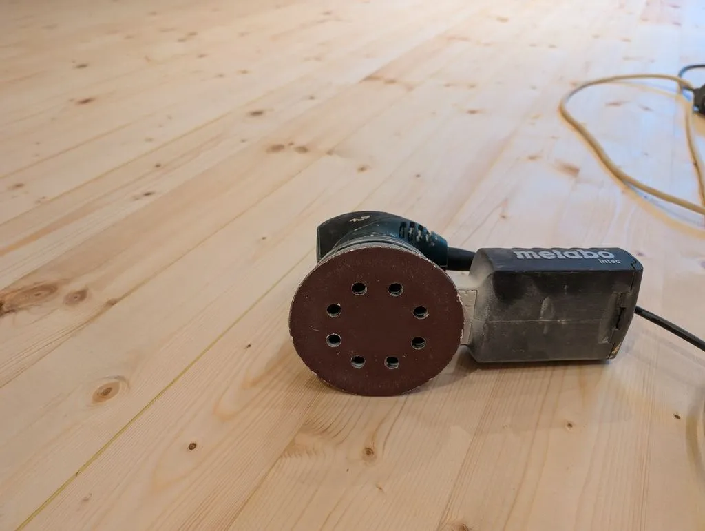 The floor is sanded briefly with a high-grit sandpaper between every coat of sealer and finish. This mechanically scuffs up the previous coat at a miscroscopic level to ensure a better bond of the next coat.