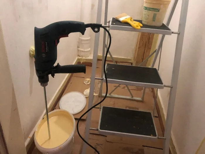 Mixing pastel yellow pigment into paint with a paddle attachment and corded electric drill.