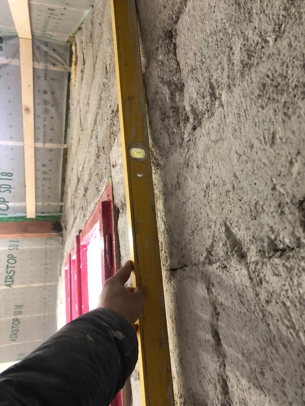 The existing wall is bowed outward—note the large gap under the straight level. We leveled this bow so as to create an approximately planar surface before applying Multipor