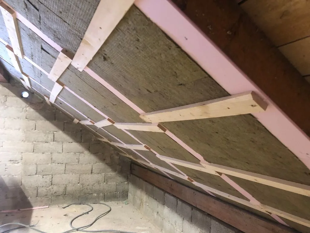 The second layer of rock wool batts (50 mm thick) placed between the rafters, flush with the XPS furring over the rafters. The wooden boards temporarily hold the batts in place until the polyurethane adhesive on the back cures (the adhesive supplements the friction fit).